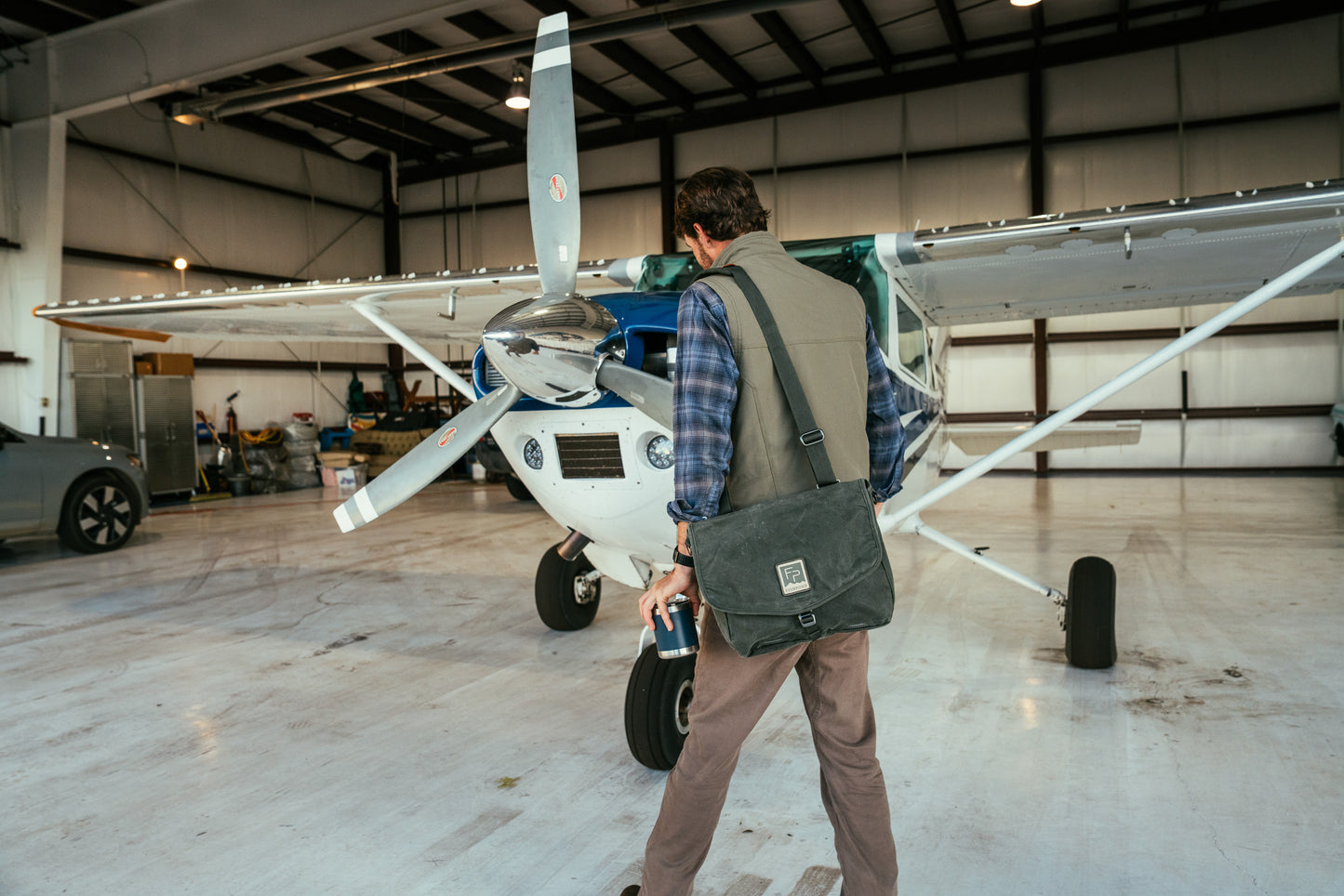 Man with a bag walking towards a small airplane in a hangar