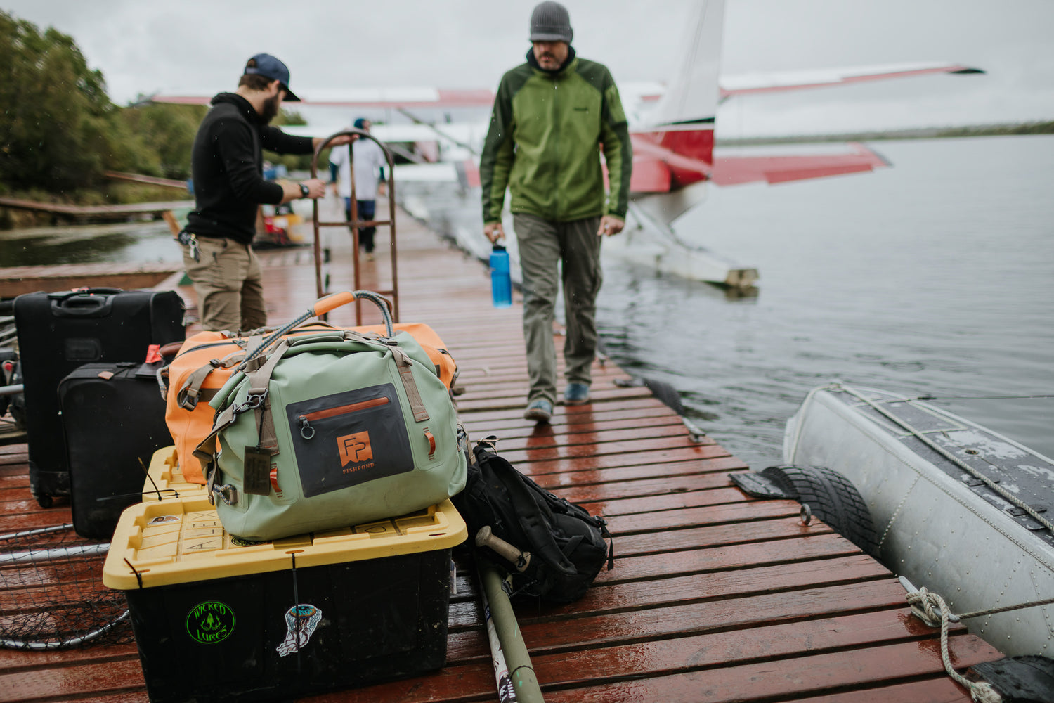 Two men with outdoor gear on a dock by a boat